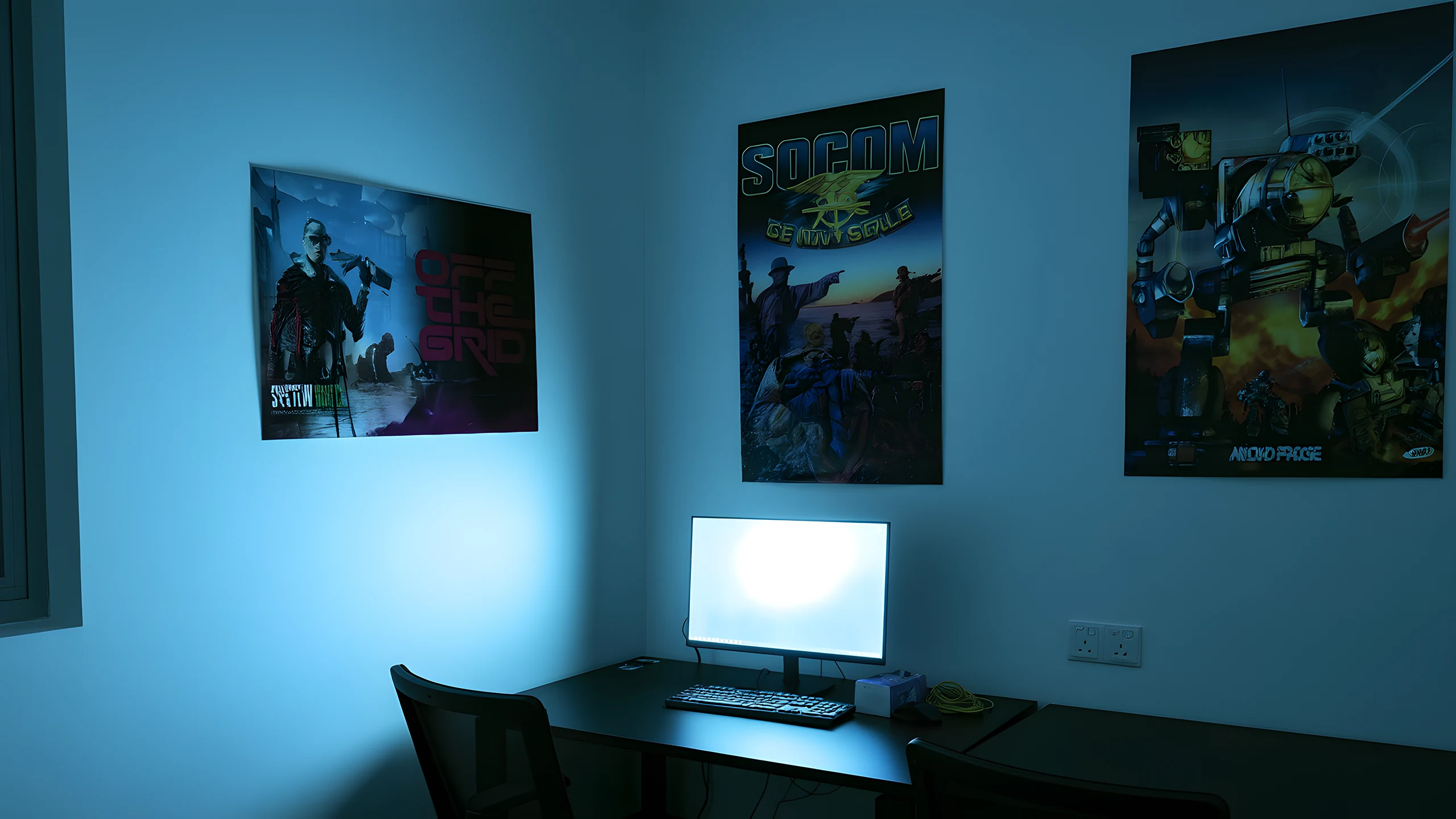 A second view of the same desk, lit blue, with framed posters above it and two mesh office chairs pushed underneath.